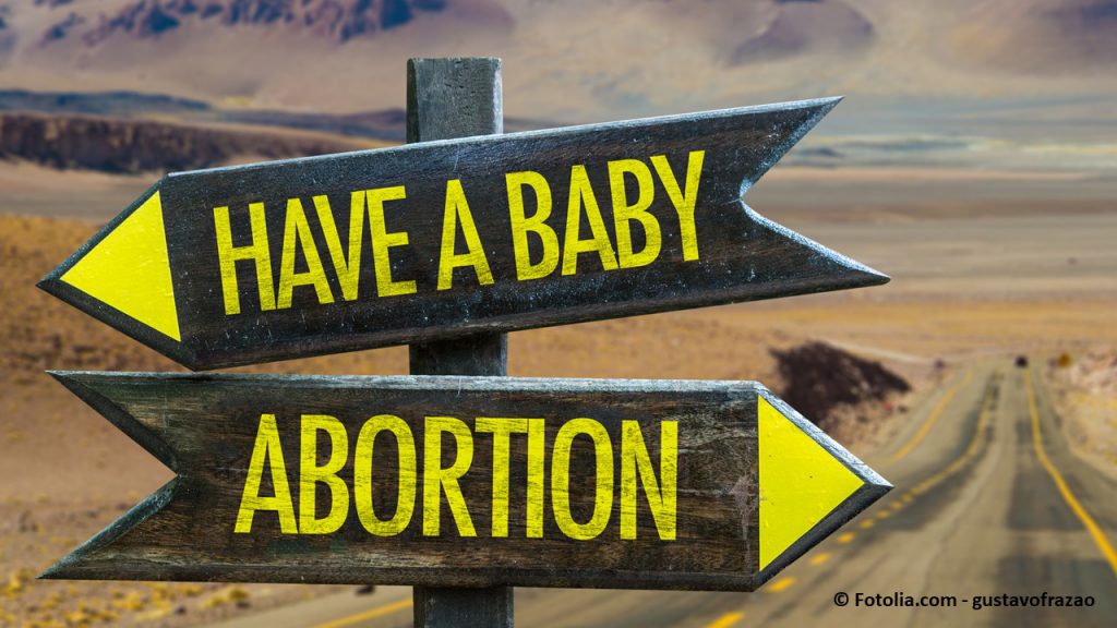 Two road signs pointing in opposite directions: Have a baby/Abortion